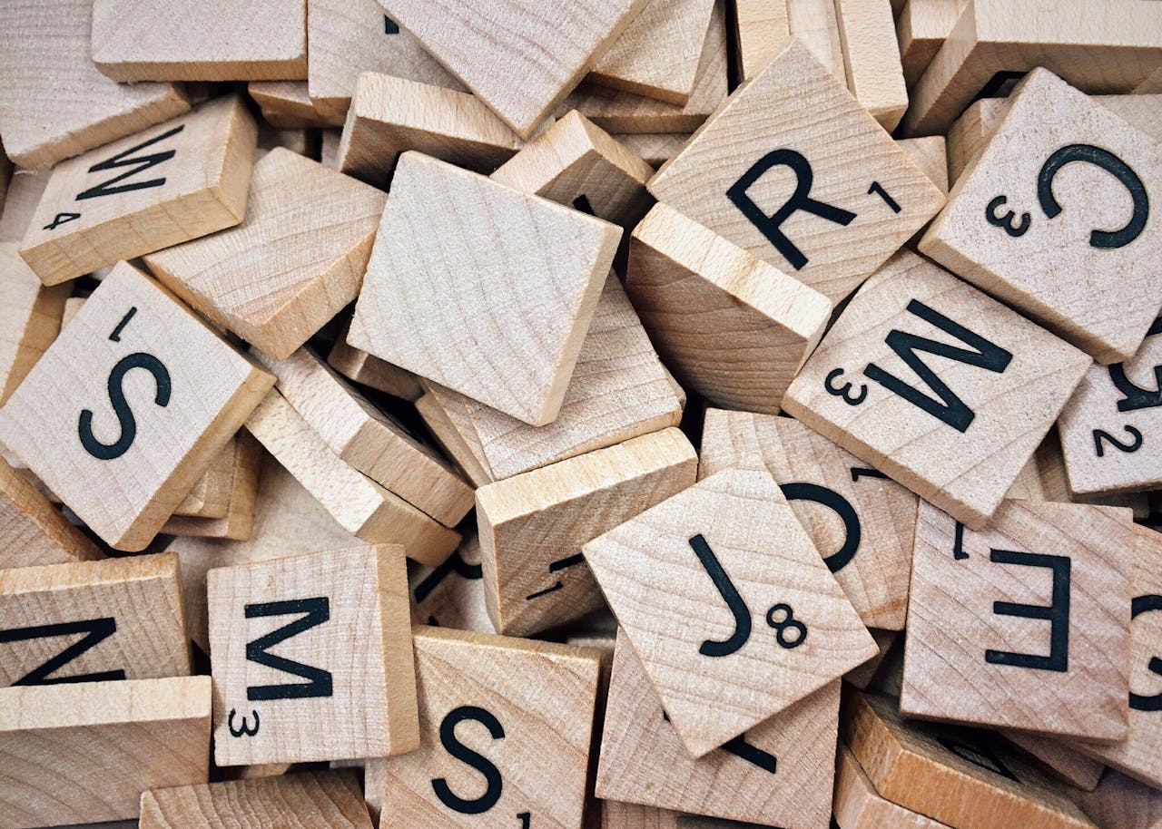 our-services-1 A collection of wooden Scrabble tiles with letters and numbers stacked randomly.