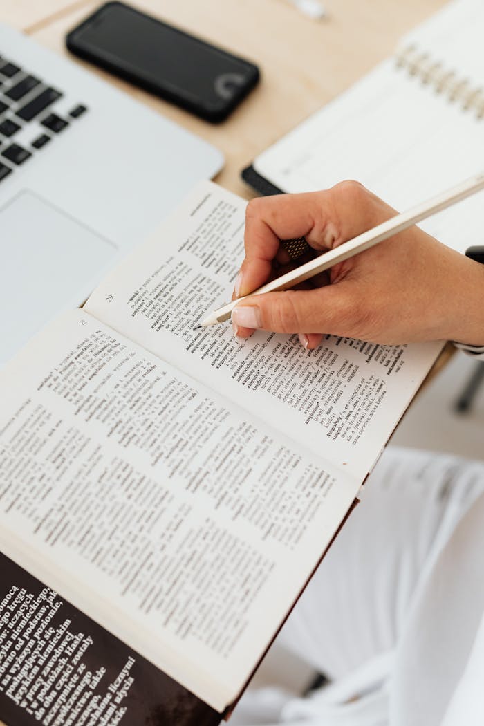 services-03 Close-up of a person underlining text in a dictionary on a desk with a laptop.